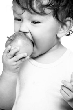 Şirin kıvırcık saçlı bebek mutlu bir gülümsemeyle lezzetli ve sağlıklı meyveler yiyor.