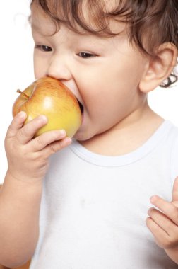 Şirin kıvırcık saçlı bebek mutlu bir gülümsemeyle lezzetli ve sağlıklı meyveler yiyor.