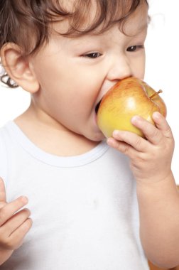 Şirin kıvırcık saçlı bebek mutlu bir gülümsemeyle lezzetli ve sağlıklı meyveler yiyor.