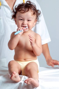 Şirin kıvırcık saçlı bebek diş fırçası ve diş macunuyla dişlerini fırçalıyor.