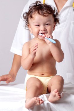 Şirin kıvırcık saçlı bebek diş fırçası ve diş macunuyla dişlerini fırçalıyor.