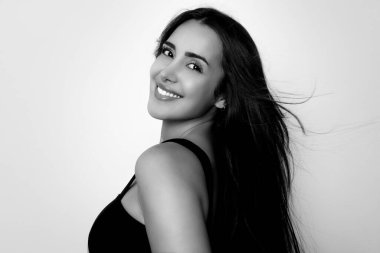 Sağlıklı, düz ve uzun siyah saçlı, mutlu bir gülümsemeyle poz veren güzel bir genç kadın.