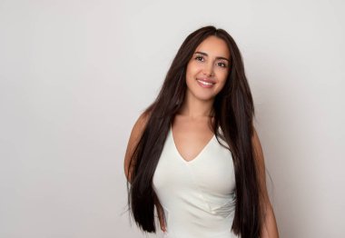 Sağlıklı, düz ve uzun siyah saçlı, mutlu bir gülümsemeyle poz veren güzel bir genç kadın.