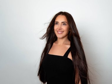 Sağlıklı, düz ve uzun siyah saçlı, mutlu bir gülümsemeyle poz veren güzel bir genç kadın.