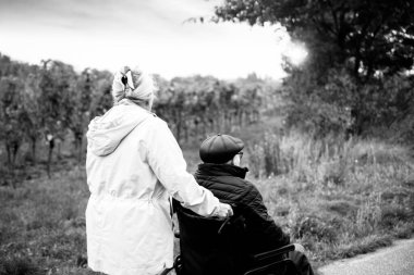 Yaşlı bir çift tekerlekli sandalyenin yardımıyla parkta yürüyüş yapıyor.