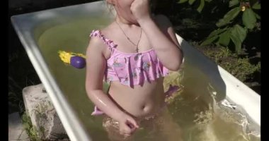 Child girl bathe in summer in a bathtub in the garden. In Visiting the village and grandparents.