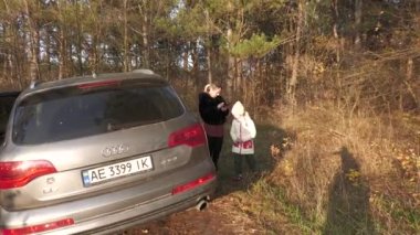 Ukrayna, Novomoskovsk şehri, 29 Ekim 2022. Bir aile, sonbaharda, güneşli ve güzel bir sonbahar gününde sonbahar mantarları için ormanda yürür. Büyük bir Audi Q7 SUV ile..