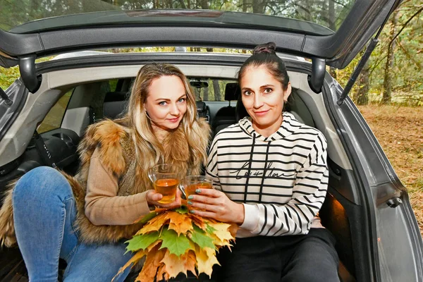 Women drink tea in the autumn forest in the trunk of a car.