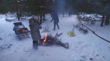 Karlı bir çam ormanında kışın ızgara kebap yapan iki aile..