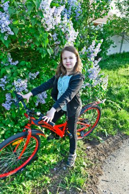 A child girl rides a bicycle in the spring in the village. clipart