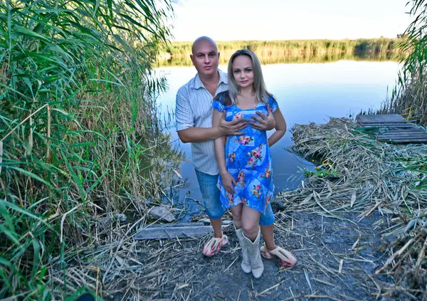 Beautiful couple man and woman, husband and wife kissing on the shore of a lake outside the city on a summer evening.