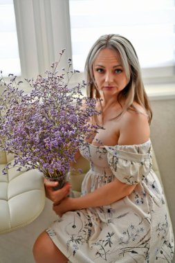 Güzel, seksi bir elbise içinde, bir buket güzel sonbahar çiçeğiyle, deri bir bar sandalyesinde poz veren seksi bir kadın..