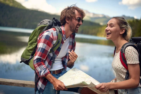 湖のそばで自然の中で笑って地図を持っている若い大人の白人夫婦は — ストック写真