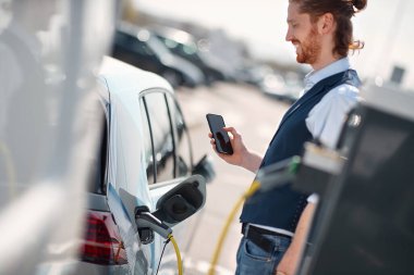 Benzin istasyonunda yakıt ikmali yapan cep telefonlu bir adam.