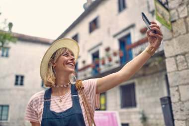 Selfie zamanı. Cep telefonlu genç bir kadın sokakta selfie çekiyor. Yaşam tarzı, moda, tatil konsepti.