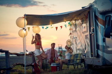 Bir grup arkadaş kampta oturuyor ve güzel bir gün batımında içiyorlar. Tatil, arkadaşlık, kamp, doğa