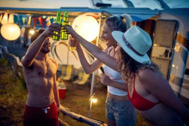 Neşeli arkadaşlar birayla kadeh kaldırıyor. Kampçının önündeki genç hippiler birlikte eğleniyorlar. Seyahat, hafta sonu, birliktelik, yaşam tarzı konsepti.