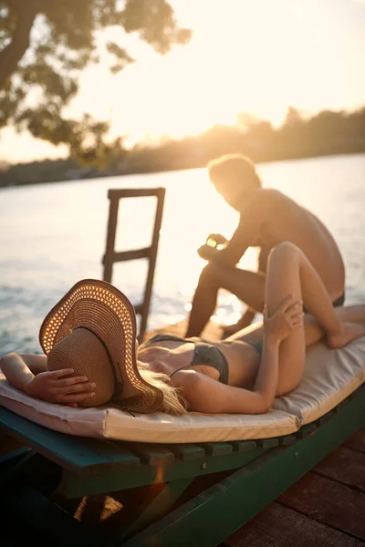 木製の桟橋で海の水着でカップル 若い男と女の日光浴 ライフスタイルの概念 — ストック写真
