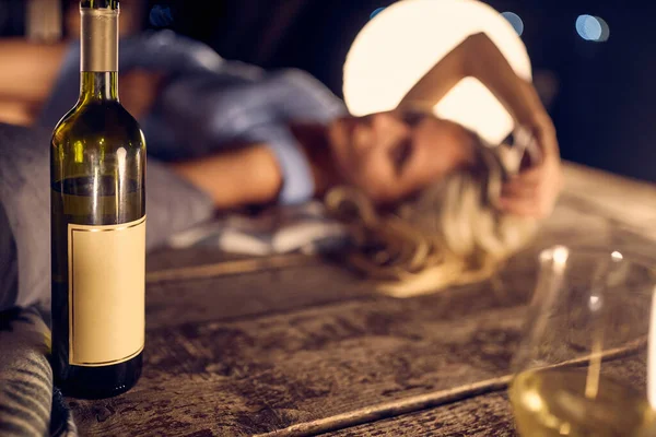一壶白葡萄酒成了焦点 晚上在户外的木制防水堤上约会 模糊的妇女躺在背景中的形象 生活方式概念 — 图库照片