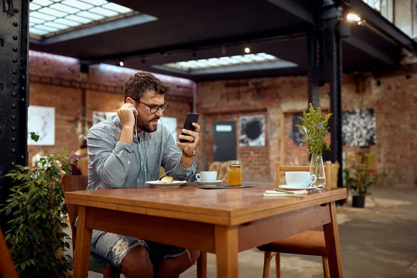 咖啡店里的男人在看他的手机 在听耳机 咖啡休息时间 — 图库照片
