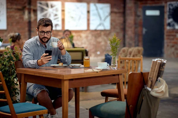 Yakışıklı Genç Bir Erkek Kafede Oturuyor Müzik Dinliyor Telefonda Kayıyor — Stok fotoğraf