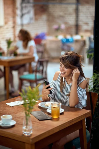 Piękna Uśmiechnięta Młoda Kobieta Słuchawkami Kawiarni Rozmawiająca Przez Telefon Nowoczesne — Zdjęcie stockowe
