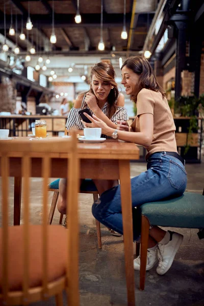 Молоді Щасливі Подружки Насолоджуються Кавою Разом Дивлячись Телефон Розмовляючи Сміючись — стокове фото
