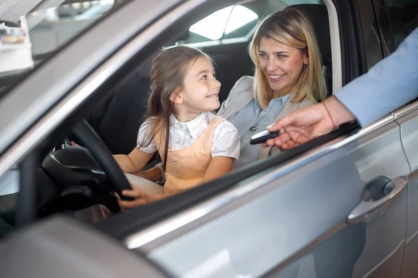 幸せな若いです女の子とともにお母さんホールディングAホイールの新しい車で販売サロ — ストック写真