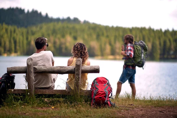 友人のグループは 湖の横に美しい日に山をハイキングの休憩中に座っている ハイキング — ストック写真