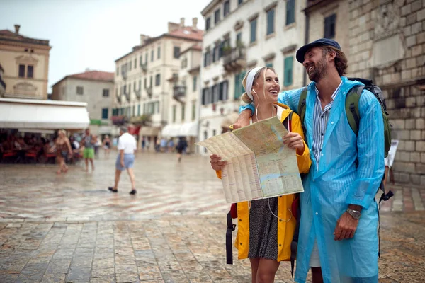 在海滨的一个雨天 一对年轻夫妇正在用地图在一座古城散步 — 图库照片