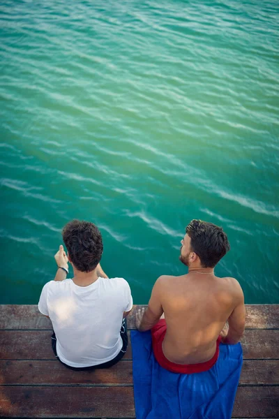 Two Young Men Sitting Wooden Jetty Looking Water High Angle — Stock Photo, Image