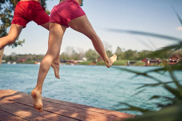 水に向かって木製の桟橋にジャンプ手を保持カップルの背面ビュー 一緒に楽しい時間を過ごすことができます ライフスタイルの概念 — ストック写真