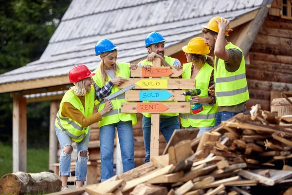 年轻的建筑工人为木桌 集体工程欢呼 在木制房屋骨架上工作的建筑工人微笑 建筑业 房地产 团队精神概念 — 图库照片