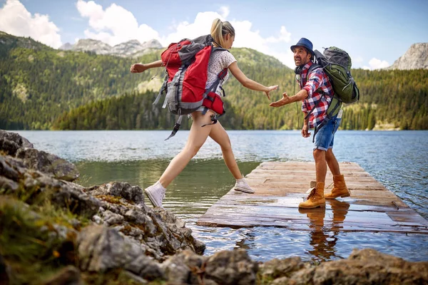 湖で木製の桟橋に若いカップル 女性のジャンプ 男は彼女に手を貸す ライフスタイル 自然概念 — ストック写真