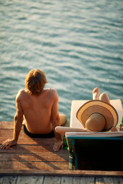 木製の桟橋でカップル日光浴 男が座って 女性は日なたぼっこをしている 夏休みのコンセプト — ストック写真