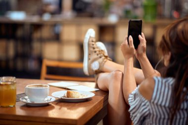 Cep telefonlu, ayakları havada, kulaklık takan, kafede eğlenen genç bir kadın.. 