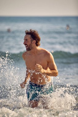 Çılgın mutlu adam sahilde suda koşuyor.