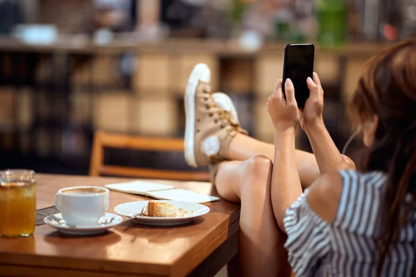 휴대폰을 여자가 다리를 탁자에 이어폰으로 카페에서 시간을 보내고 있습니다 — 스톡 사진