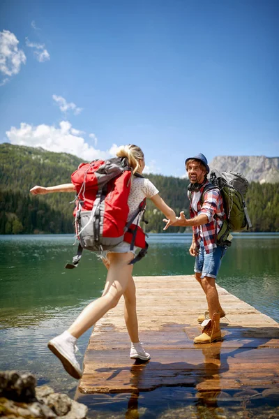 若いカップルは 美しい日に山のハイキング中に湖のドックで楽しい時間を過ごしています ハイキング — ストック写真