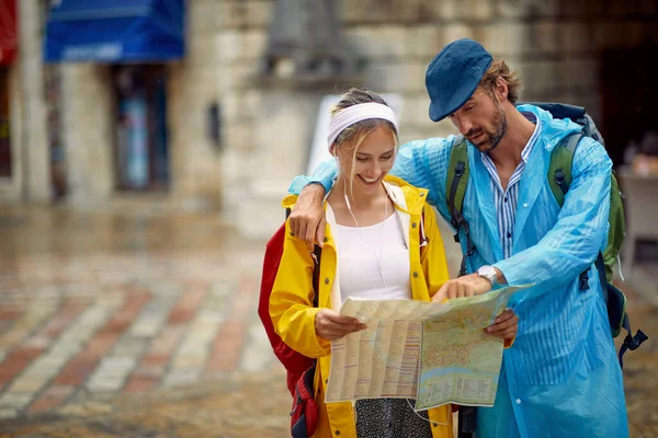 Young smiling man and woman in  raincoat walks through the old city streets on rainy da