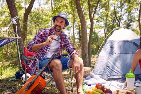Joven Hipster Hombre Sonriendo Sentado Silla Disfrutando Acampar Naturaleza Picnic —  Fotos de Stock
