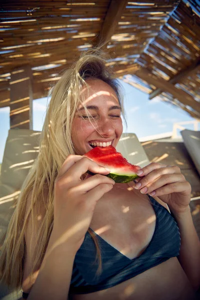 水着で陽気ブロンドの女性スイカの果物を食べて 至福感 休暇中の若い女性 楽しみ ライフスタイルのコンセプト — ストック写真