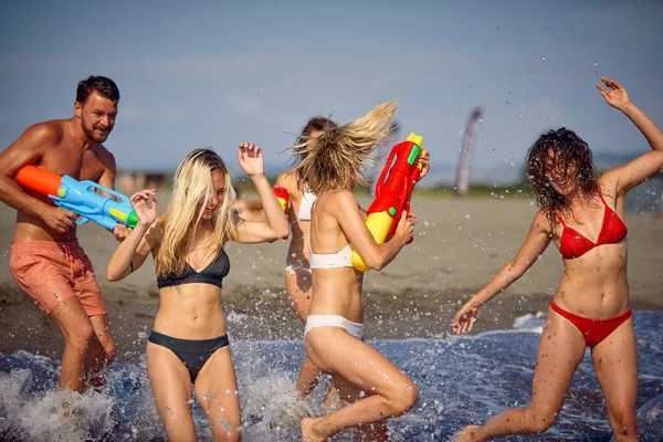友人のグループは ビーチで水のピストルで遊んでいる 夏休みに一緒に若い大人 楽しみ ライフスタイルのコンセプト — ストック写真