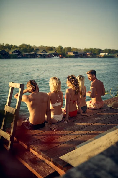 Five Young Adults Sitting Wooden Jetty Swimsuits Sunbathing Rear View — Stock Photo, Image
