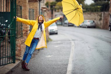 Yağmurluk giymiş, dışarıda şemsiyesi olan neşeli genç bir bayan.