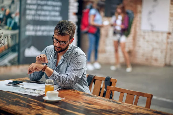 Mladý Podnikatel Brýlemi Sedí Sám Kavárně Dívá Hodinky Vychutnává Kávu — Stock fotografie