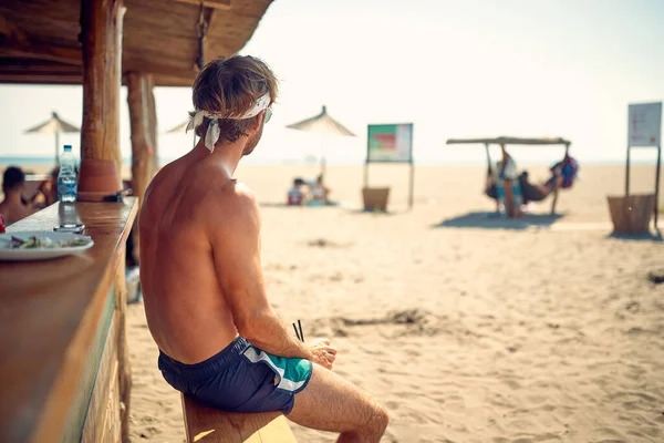 ハンサムな若い男のビーチのバーで離れて水を見て座っての背面ビュー 夏休みの男 レジャー ライフスタイル 休日のコンセプト — ストック写真