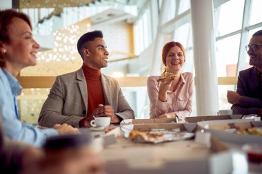 Bir grup güler yüzlü iş adamı lokantada yemek yiyor ve konuşuyor.