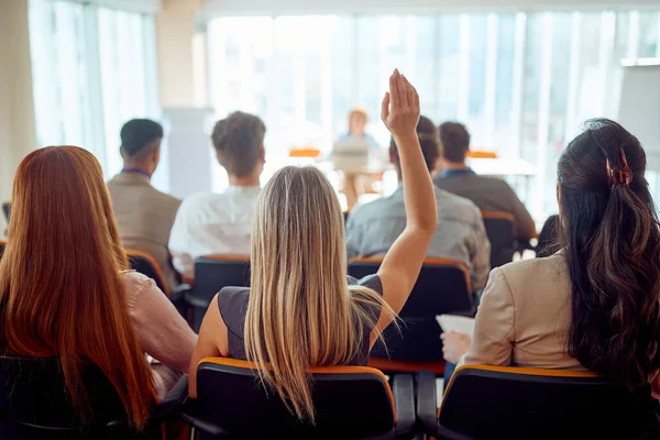 若い女性参加者が会議室の作業環境でビジネス講演中に質問をするために手を挙げています ビジネス — ストック写真