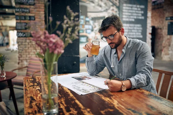眼鏡をかけ カジュアルな服装の若者がカフェで新聞を読んで 一人で座っている モダンなカフェインテリア — ストック写真